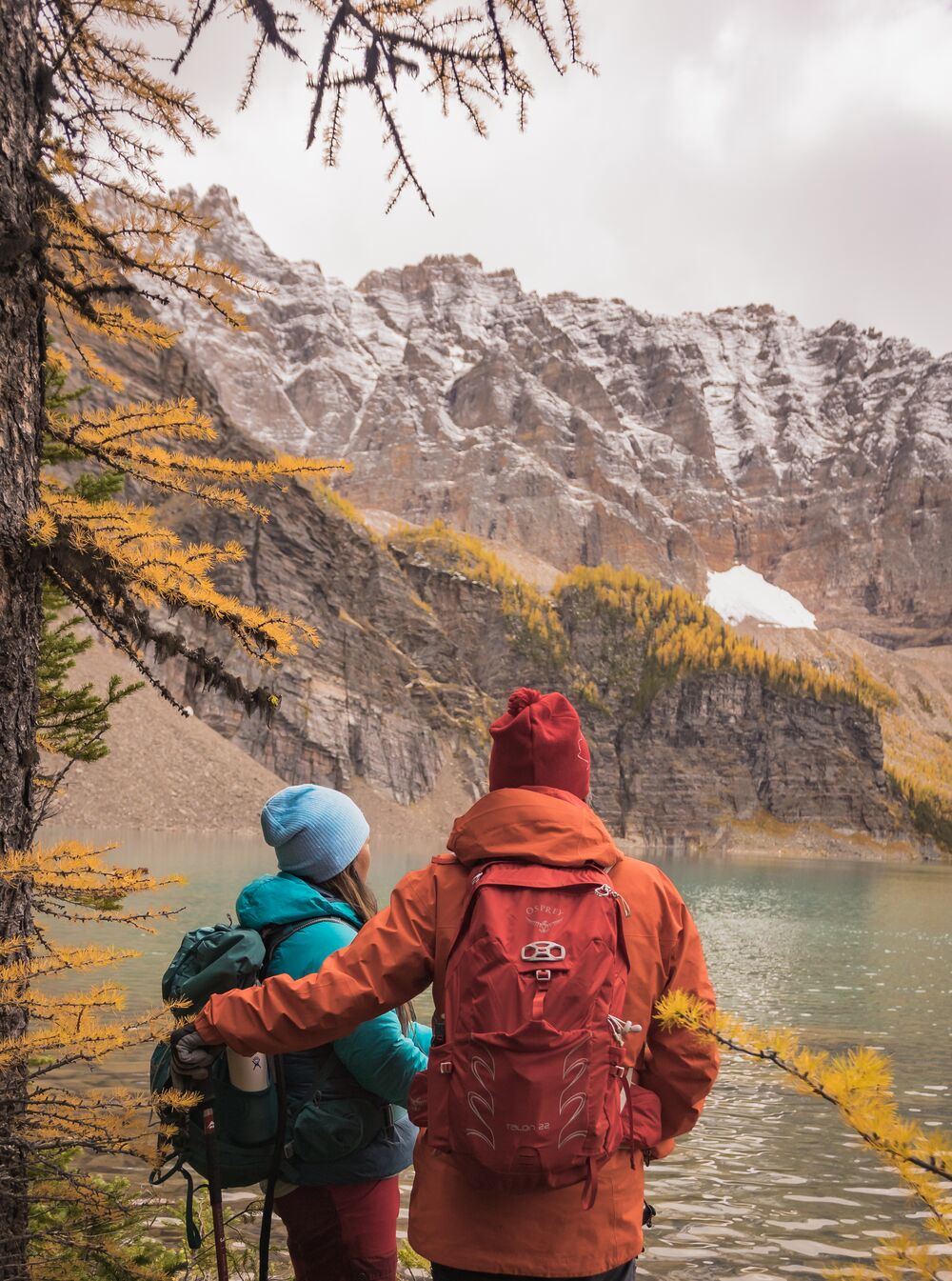 Two people stand looking at larches at Taylor Lake in Banff National Park.